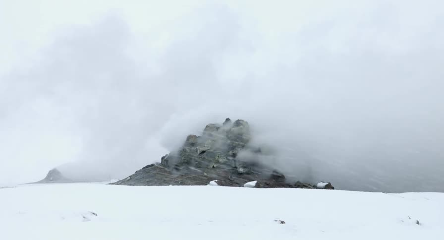 Heavy snow is falling over rocks with steam rising from geothermal activity
