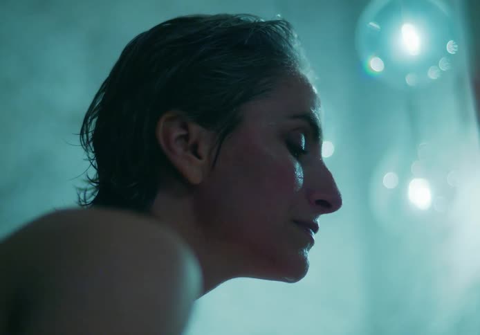 A woman bathing sits up as water drips from her face and she wipes her eyebrow