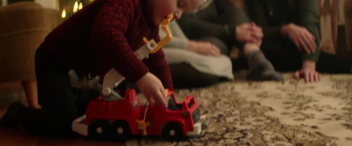 Family gathered for the christmas holiday watches boy play with toy fire truck