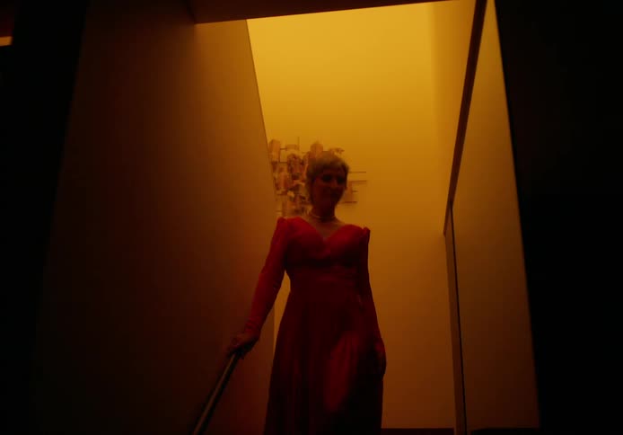 A woman is descending a staircase in her home wearing an evening gown at night