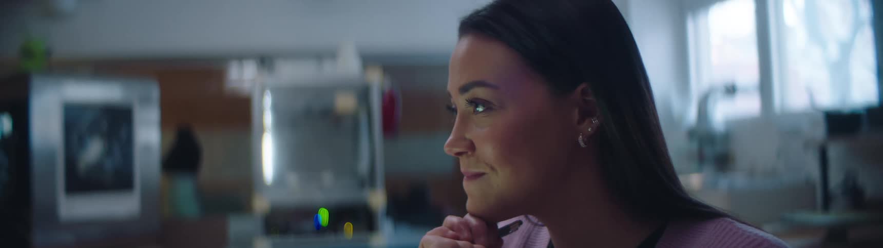 A woman sitting working and thinking in a lab smiles then gets back to work