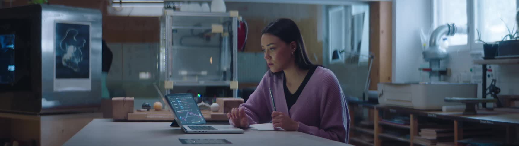 A young woman sits at a desk and works on a laptop as she thinks