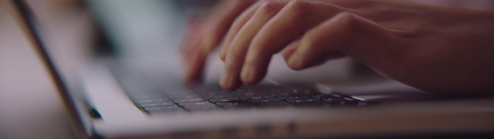 A persons hands are seen up close as they are quickly typing on a laptop keyboard