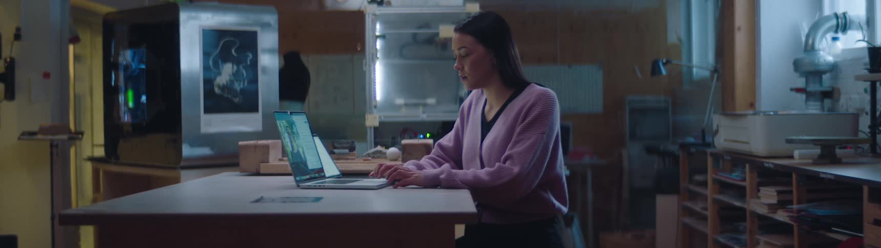 A woman uses a laptop to participate in a video chat while sitting at a table in a workshop