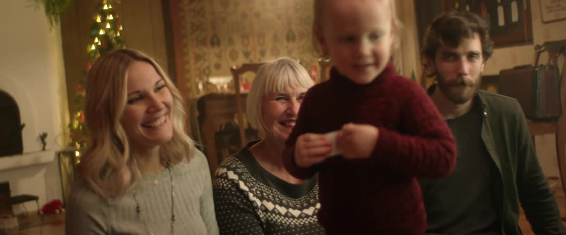 Family sitting on the living room floor looking at a baby dancing at christmas