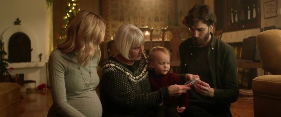 A grandmother sitting with her grandson and their parents indoors at christmastime