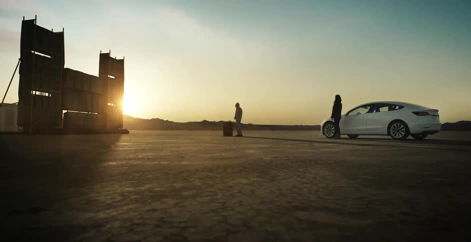 Two people are standing by a car outdoors at dusk