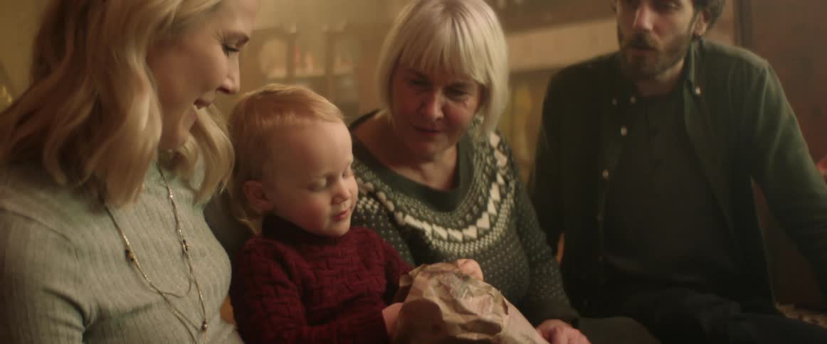 A little boy unwraps a stuffed animal and smiles as mom dad and grandma look on