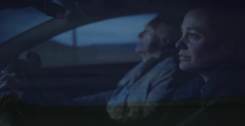 A man and woman are sitting in a car together at night