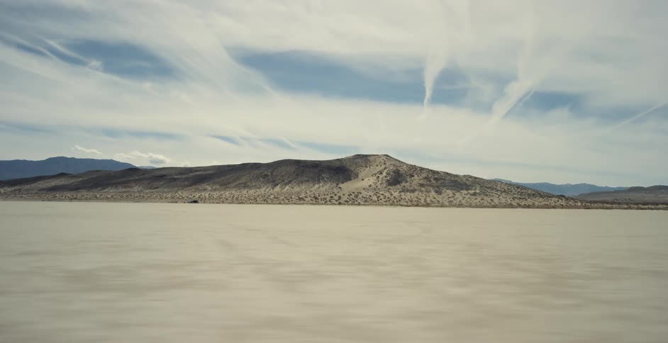 Mountains are across the desert and there are silhouettes of mountains on the horizon under a cloudy sky