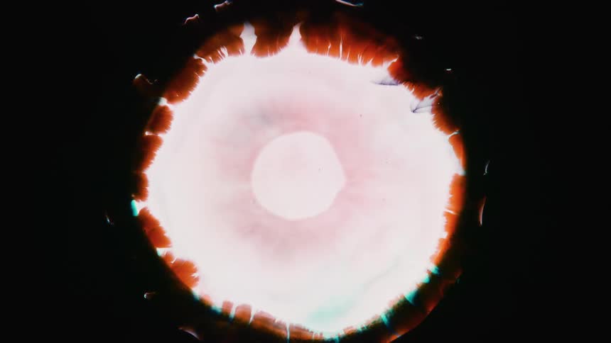 A turquoise and orange sphere bursts out of the darkness and white emerges from the center before it collapses into an orange lightning bolt