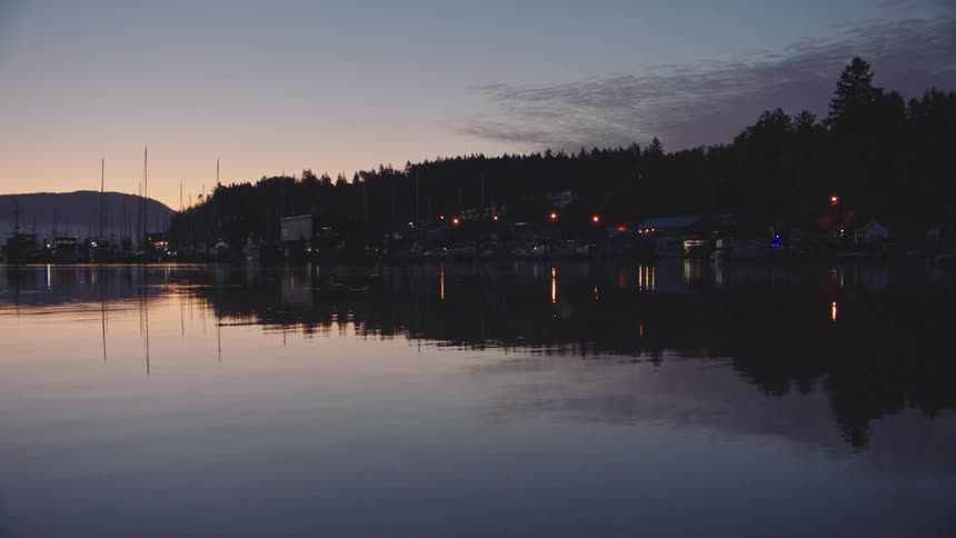 A marina seen in pre-dawn light with houses reflecting on the water
