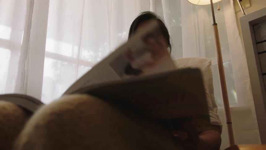 Pregnant woman with white shirt sits in armchair and turns pages of book
