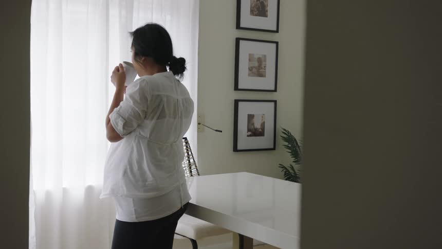 A woman is drinking a beverage while inside her home