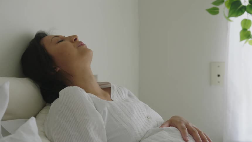 Pregnant woman reclining on bed and reading leans her head back as she strokes her abdomen