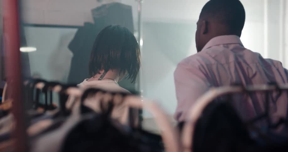 A woman helps a man try on clothing from racks
