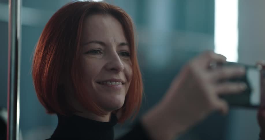 Redheaded woman takes photos with the camera on her cellphone