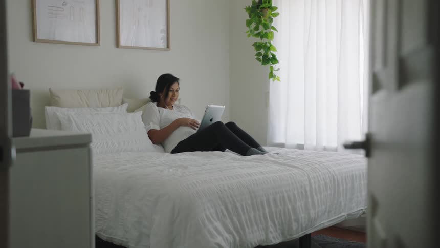 A woman uses her tablet during a video call in bed