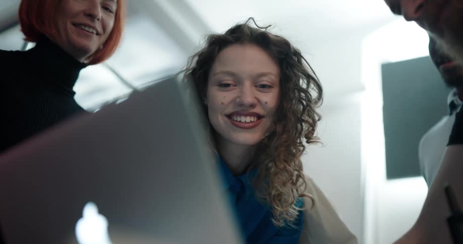 A group gathered around a laptop looking at the screen smiling pointing and talking