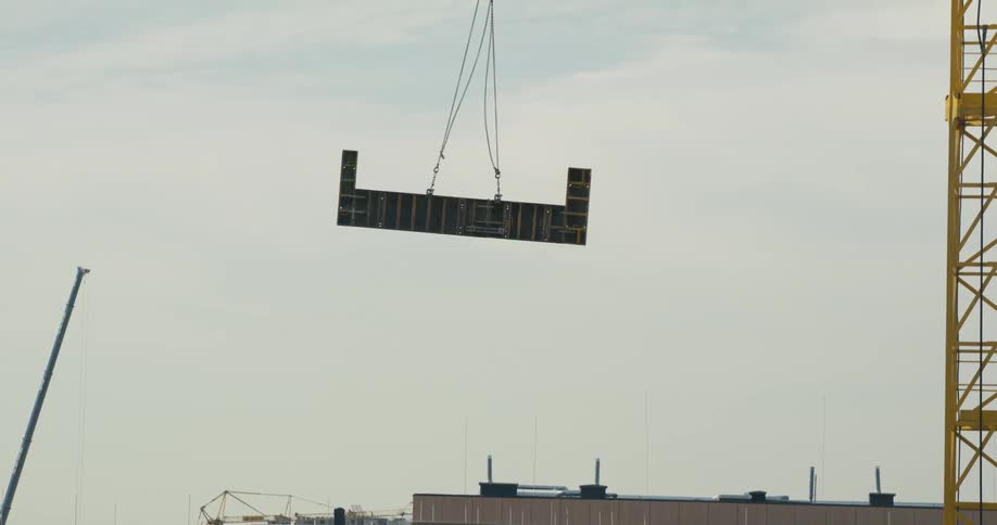 A construction crane lifts a large piece of wall up high above a building