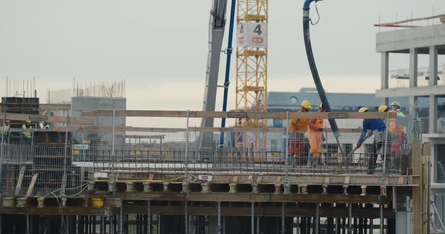 Group of workers wearing hardhats and protective equipment pouring concrete at a construction site