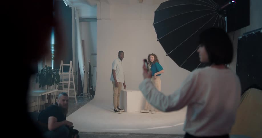 A cameraman takes photos at a photo shoot and then the two models stand up and a woman goes over and takes a selfie with her cell phone with them