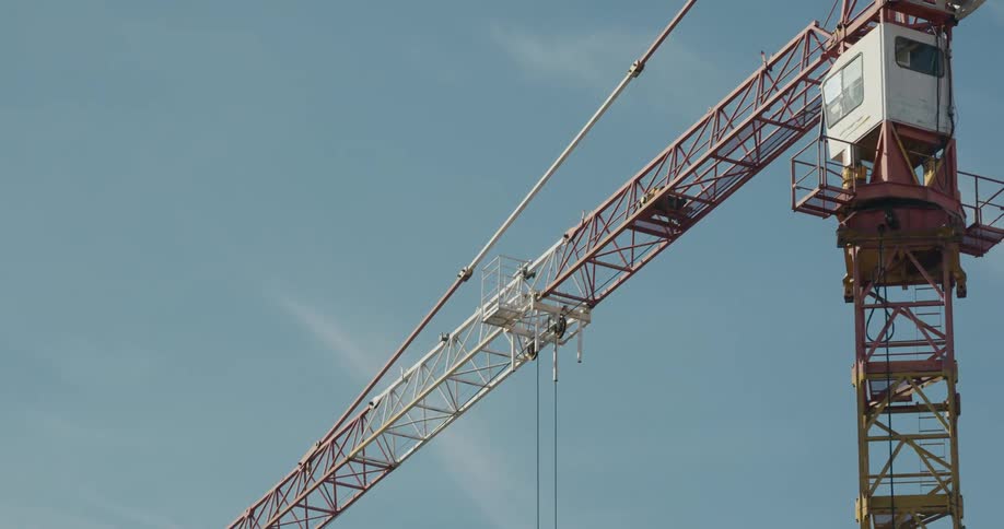 Big orange construction crane moving from right to left in front of the blue sky