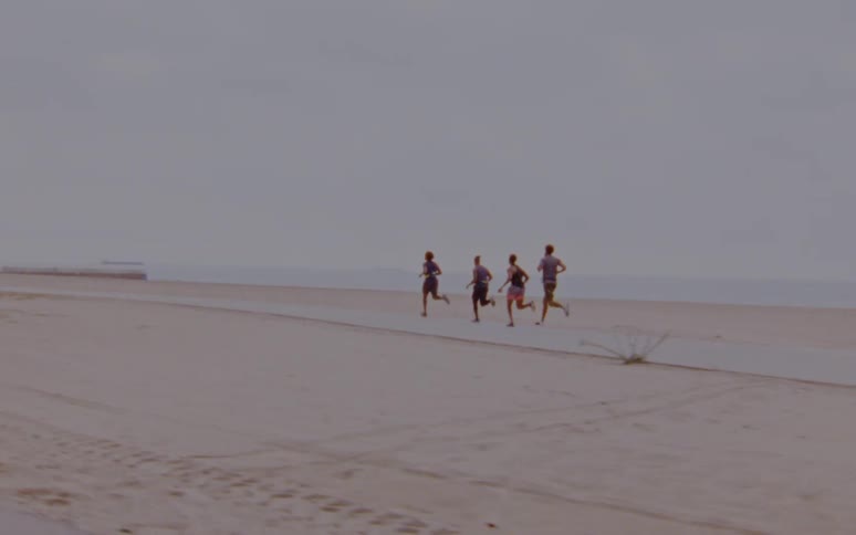 Group of people jogging on a road over the sand on a beach next to the ocean caught on vintage film