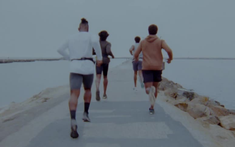 Group of people jogging on a road over the sand on a beach next to the ocean caught on vintage film