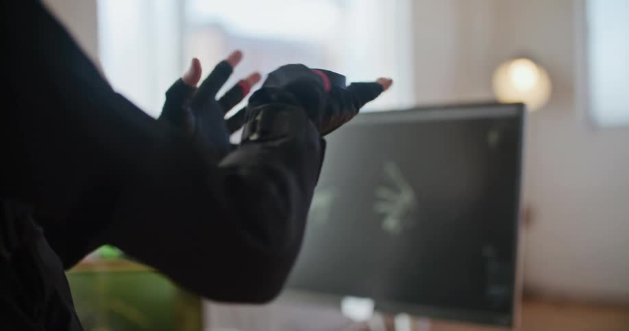 A man has virtual reality devices on his hands and his hand movements are seen on a computer monitor