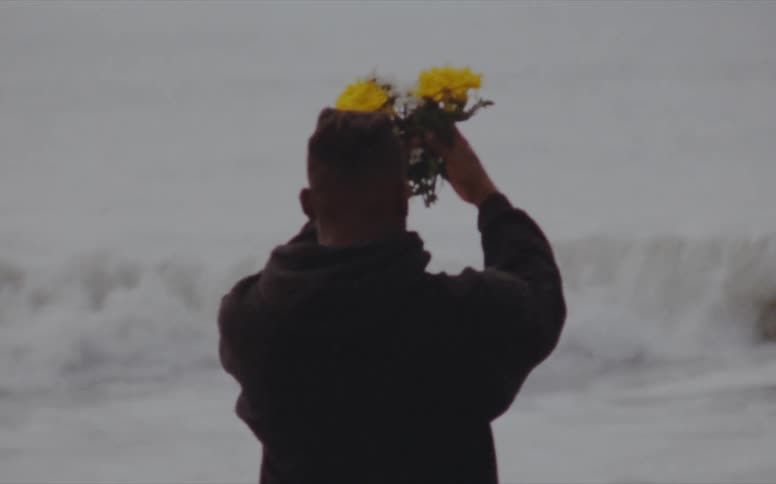 A man holds yellow flowers above his head as he performs a ceremony while standing in the ocean