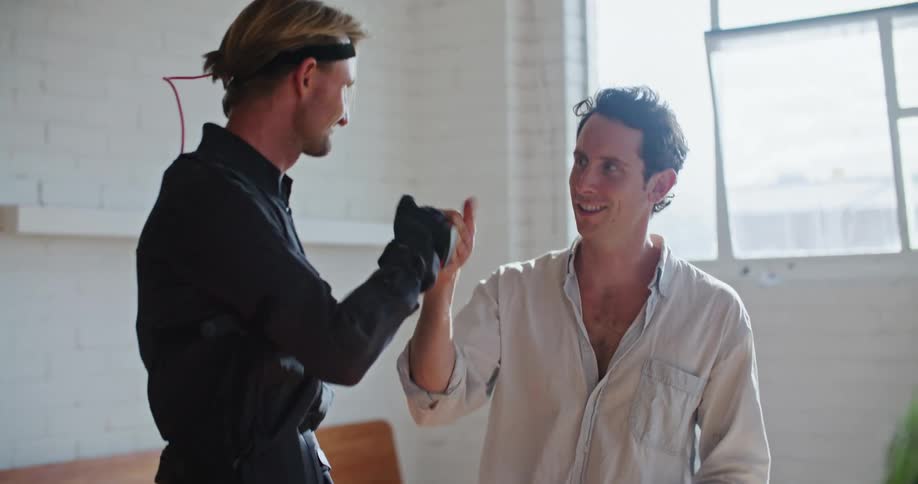 Two men discuss motion capture as one wears motion capture suit