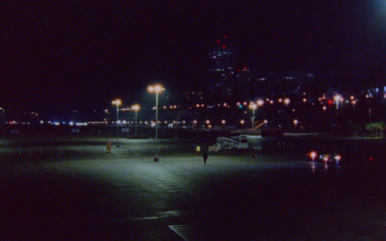 One person stretches in a parking lot at night while another person runs another person skips