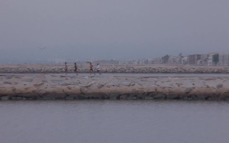 Youths run along path between town and water on misty day