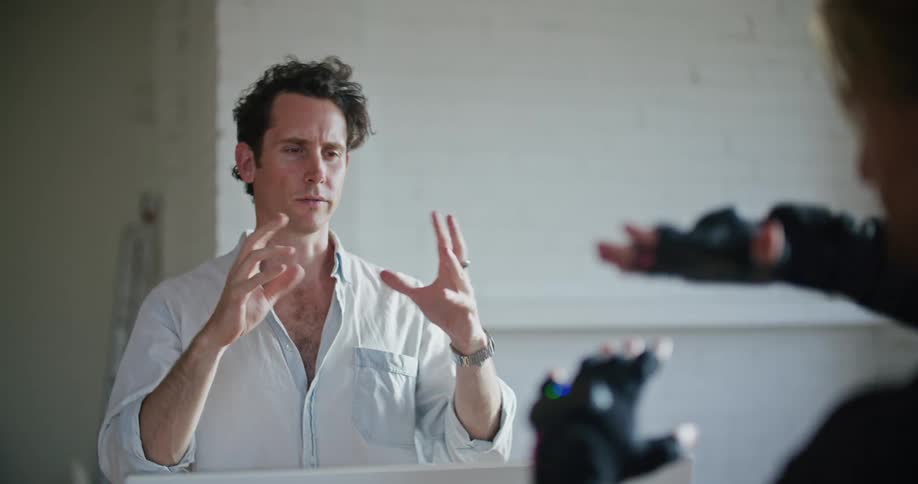 A man has interactive computer devices on his hands and another man shows him hand movements