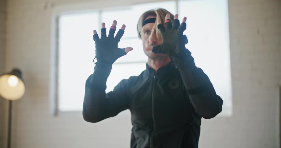 Man wearing a black motion capture suit moving into fighting poses inside a white room