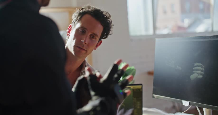 Man in white shirt gives instructions to another man wearing a futuristic motion capture black suit