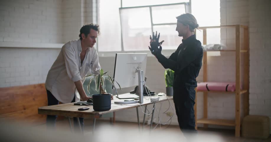 Man in white shirt gives instructions to another man wearing a futuristic motion capture black suit