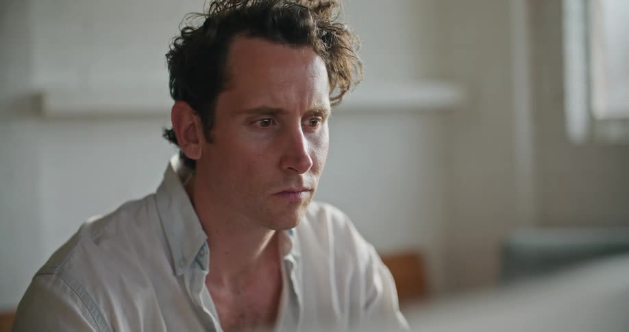 A man is sitting indoors and looking at a computer screen