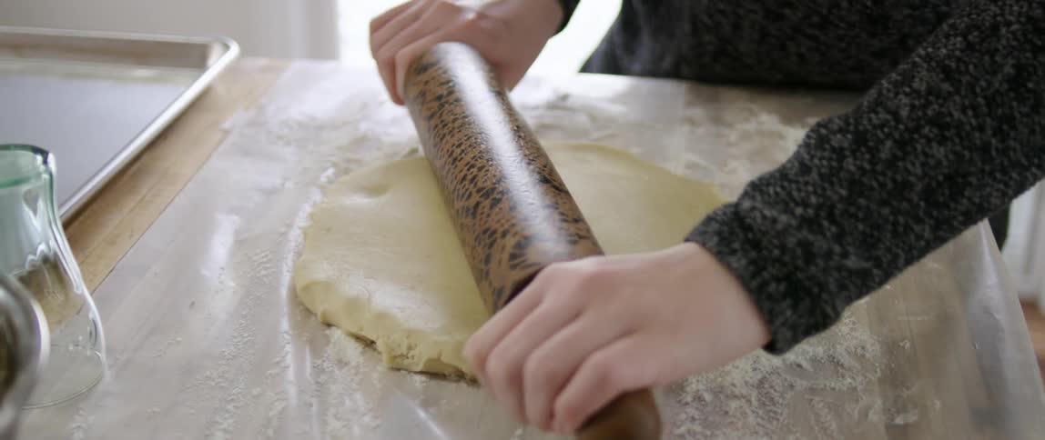 A woman uses a rolling pin to roll out some dough