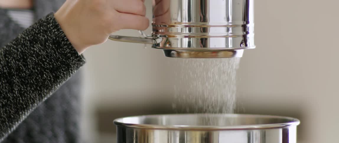 A person sifts powder into a silver bowl