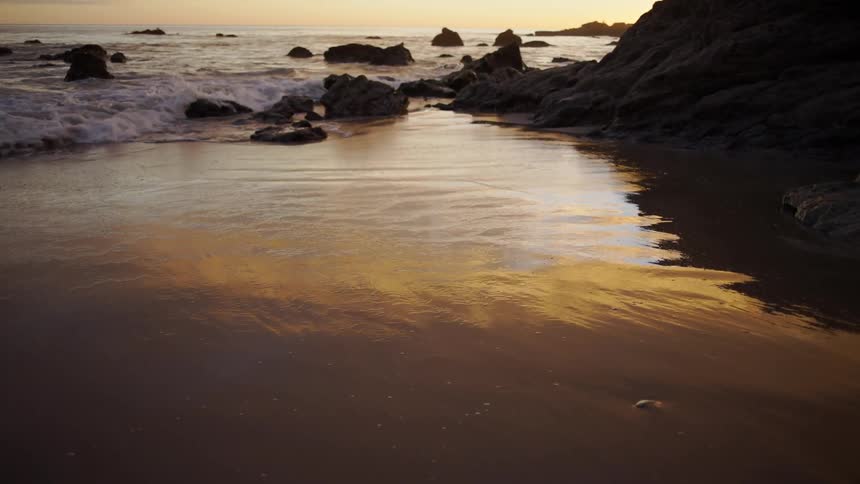 Waves roll onto wet sand reflecting red tinted sky
