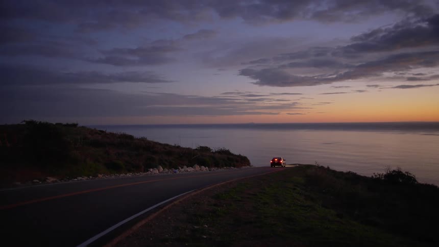 A car travels along a road towards the coast at sunset