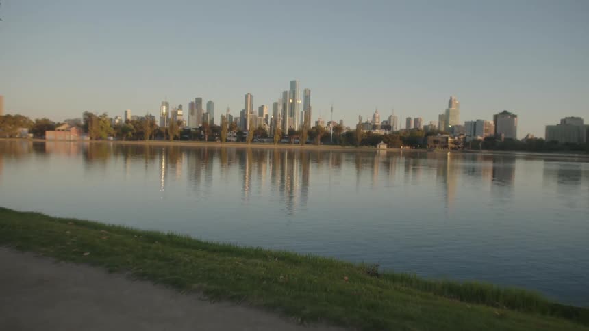 White woman wearing fitness clothing jogging in a public park next to the lake with a city skyline at the background