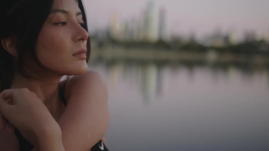 Woman stretches while standing near lake reflecting city skyline