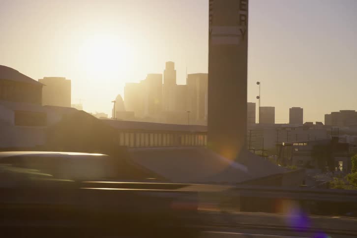 Cars drive past buildings with the skyline in the distance