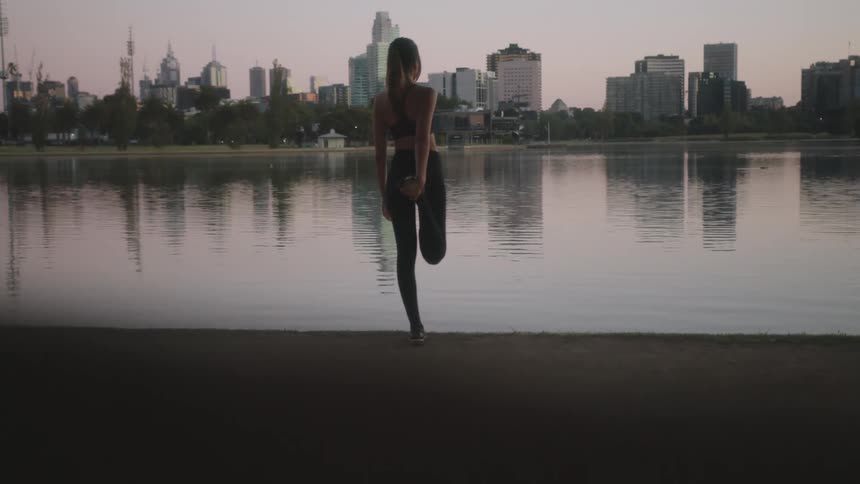 White woman wearing fitness clothing stretching and warming up in front of a lake at a public park