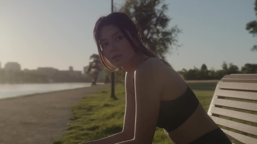 Woman wearing fitness clothing sitting down in a bench at a public park