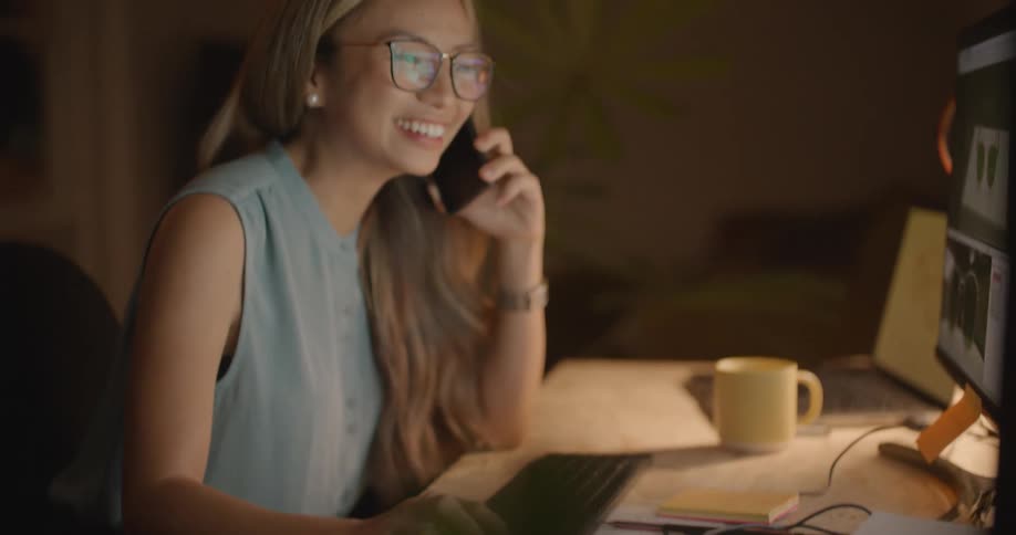 A woman is on the computer and talking on a cellphone