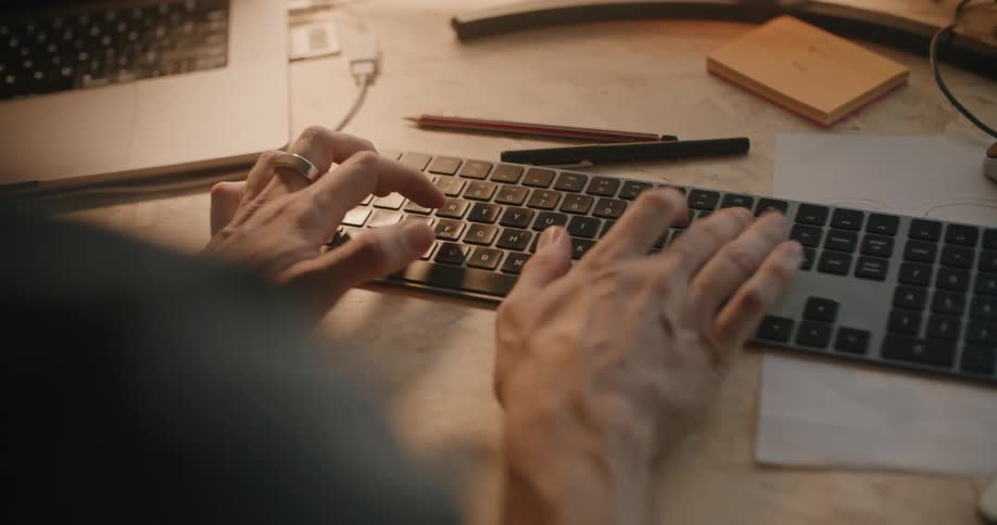 Person sits at desk near laptop typing on flat keyboard